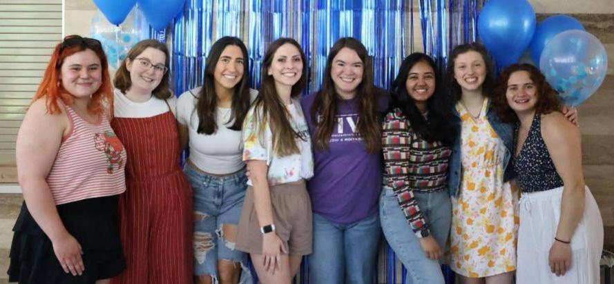 Peer educators and supervisor Katie posing for picture in front of blue backdrop and balloons